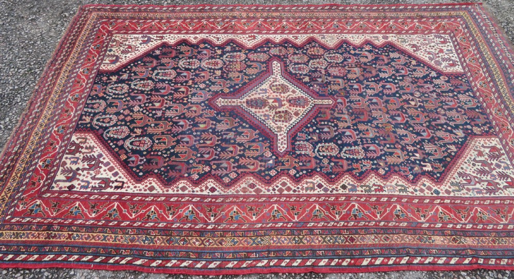 A late 19th-century Persian Qashqai hand-knotted wool rug featuring a navy blue field filled with stylized red peacock motifs, a central cream diamond medallion, and a wide red geometric border. View II