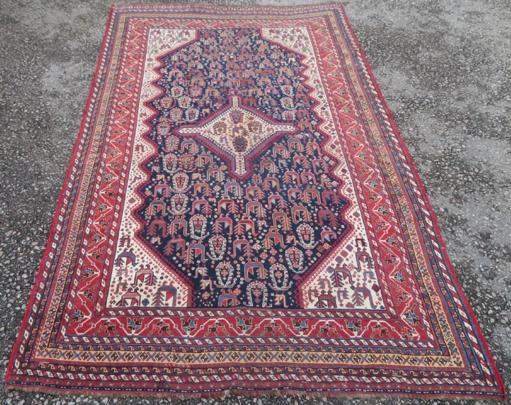 A late 19th-century Persian Qashqai hand-knotted wool rug featuring a navy blue field filled with stylized red peacock motifs, a central cream diamond medallion, and a wide red geometric border. View III