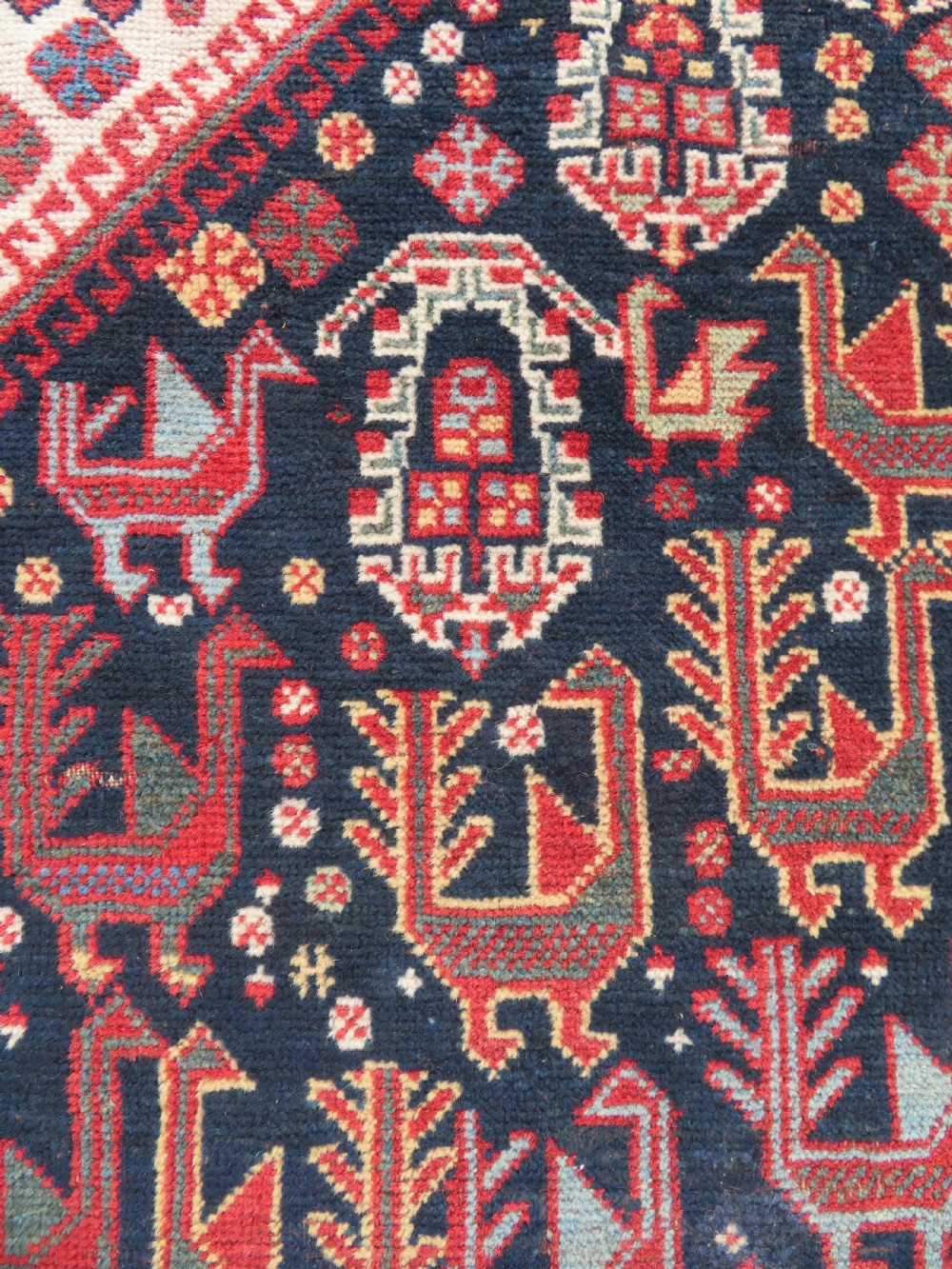 A late 19th-century Persian Qashqai hand-knotted wool rug featuring a navy blue field filled with stylized red peacock motifs, a central cream diamond medallion, and a wide red geometric border. View V