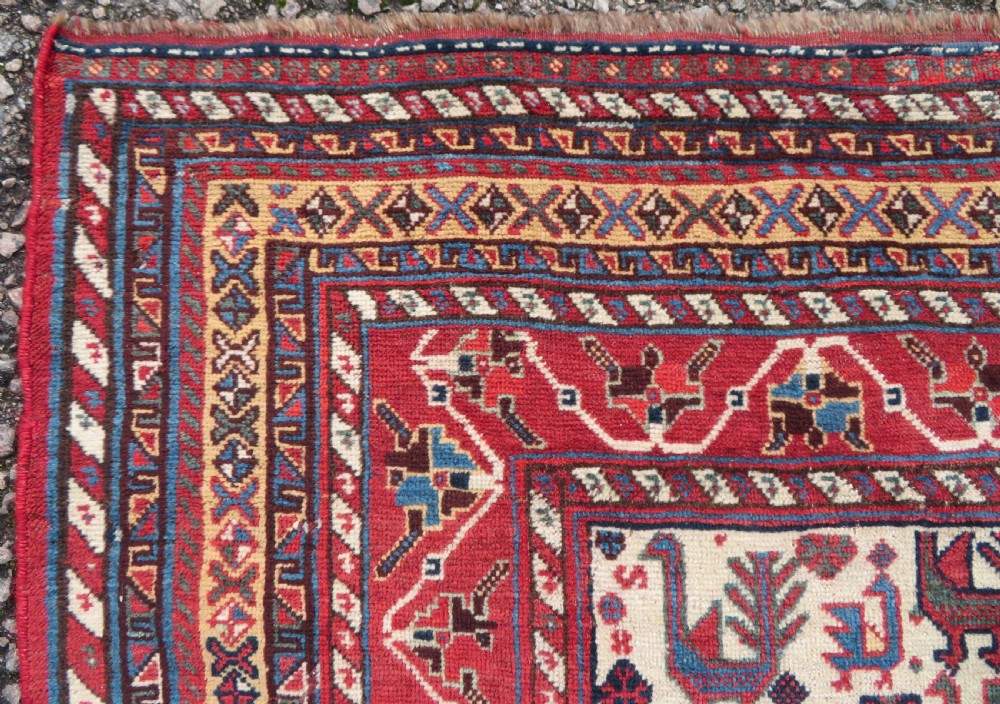 A late 19th-century Persian Qashqai hand-knotted wool rug featuring a navy blue field filled with stylized red peacock motifs, a central cream diamond medallion, and a wide red geometric border. View VI