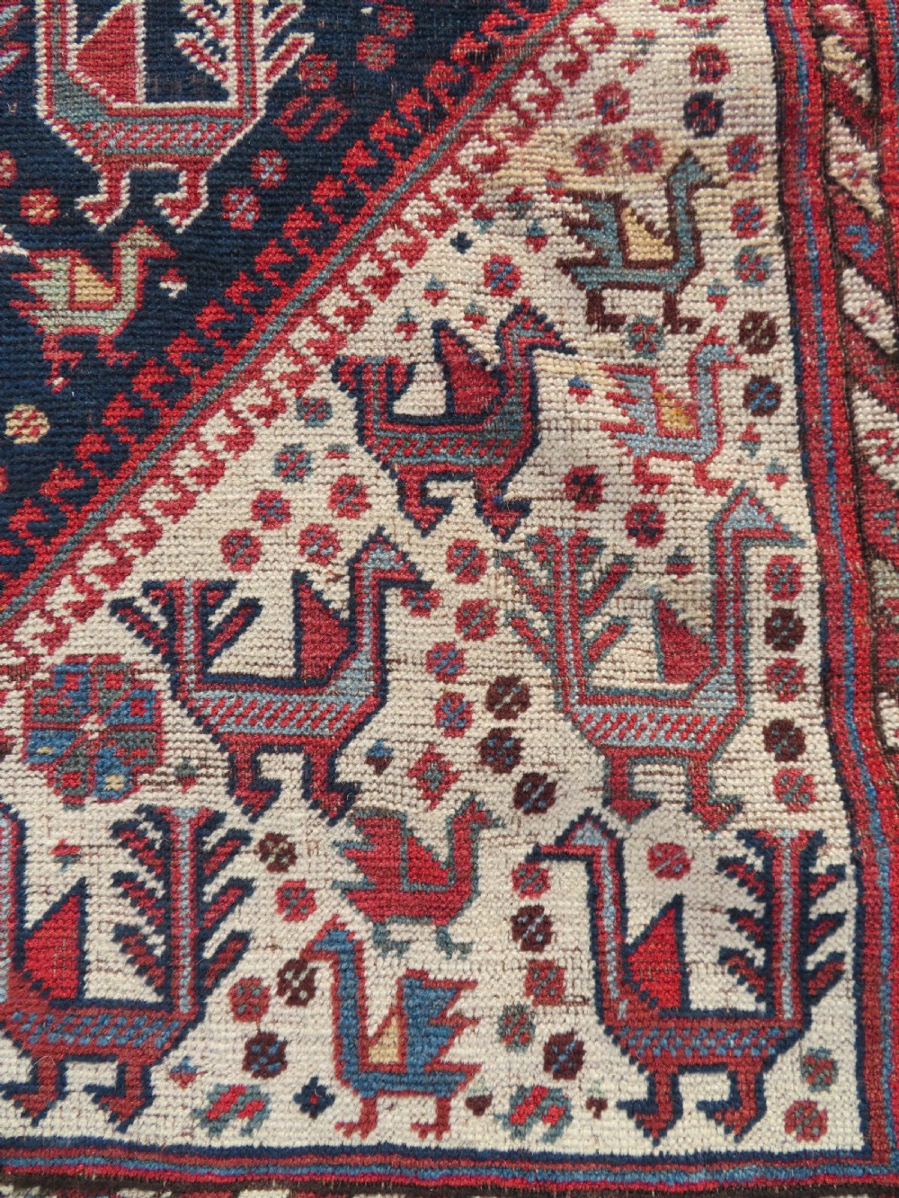 A late 19th-century Persian Qashqai hand-knotted wool rug featuring a navy blue field filled with stylized red peacock motifs, a central cream diamond medallion, and a wide red geometric border. View X