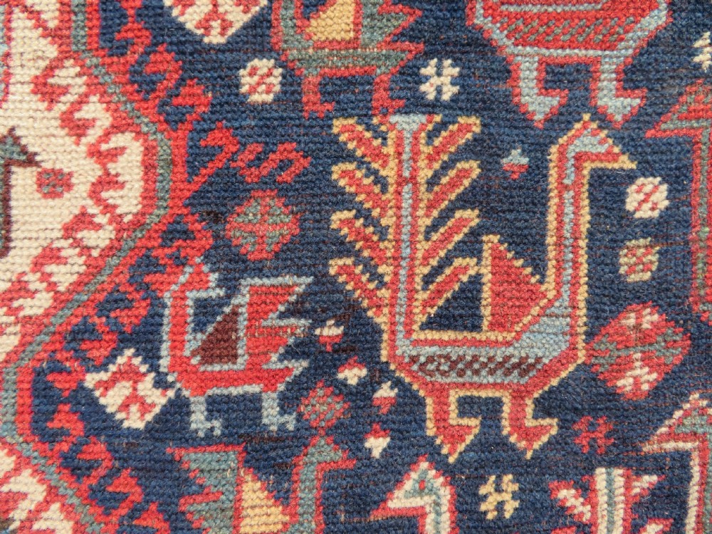A late 19th-century Persian Qashqai hand-knotted wool rug featuring a navy blue field filled with stylized red peacock motifs, a central cream diamond medallion, and a wide red geometric border. View XII