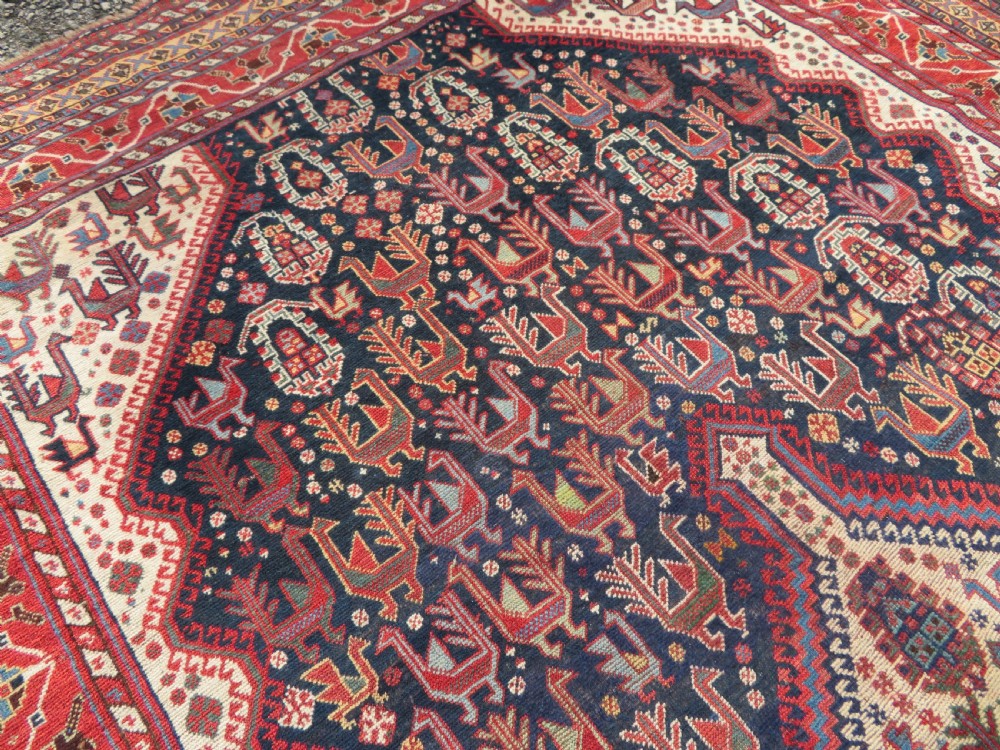 A late 19th-century Persian Qashqai hand-knotted wool rug featuring a navy blue field filled with stylized red peacock motifs, a central cream diamond medallion, and a wide red geometric border. View XV