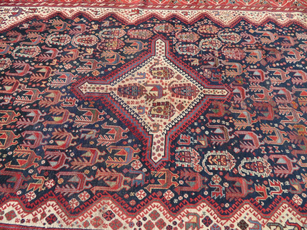 A late 19th-century Persian Qashqai hand-knotted wool rug featuring a navy blue field filled with stylized red peacock motifs, a central cream diamond medallion, and a wide red geometric border. View XVI