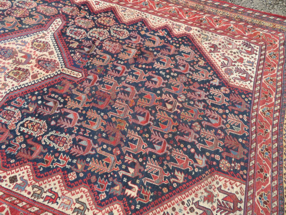 A late 19th-century Persian Qashqai hand-knotted wool rug featuring a navy blue field filled with stylized red peacock motifs, a central cream diamond medallion, and a wide red geometric border. View XVII