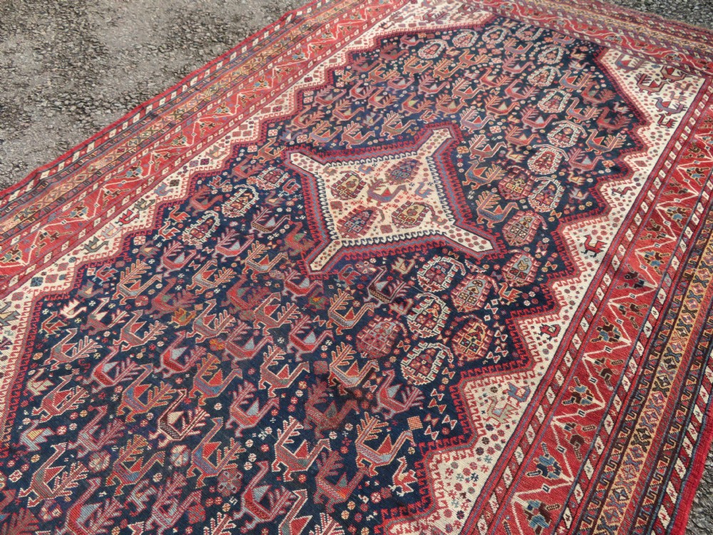 A late 19th-century Persian Qashqai hand-knotted wool rug featuring a navy blue field filled with stylized red peacock motifs, a central cream diamond medallion, and a wide red geometric border. View XVIII