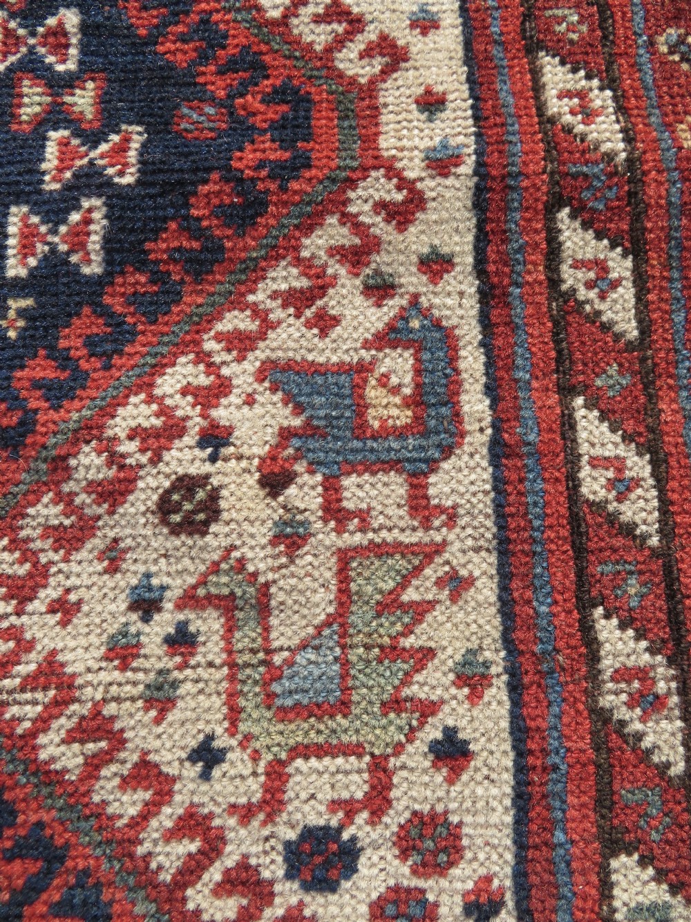 A late 19th-century Persian Qashqai hand-knotted wool rug featuring a navy blue field filled with stylized red peacock motifs, a central cream diamond medallion, and a wide red geometric border. View XXI
