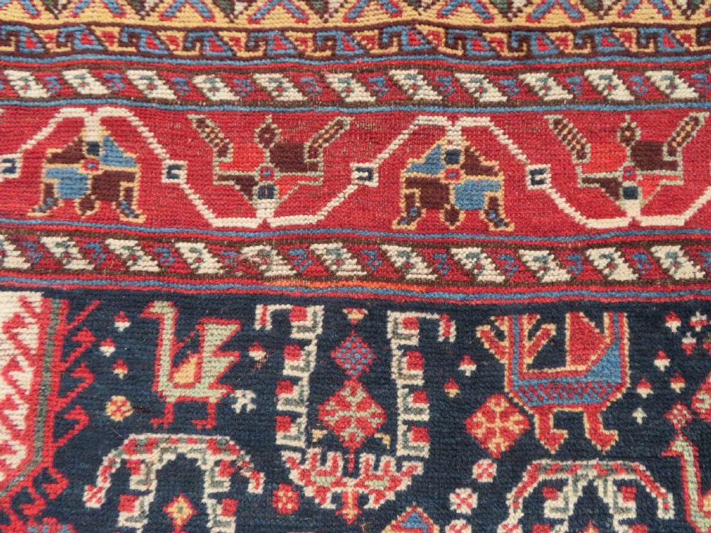 A late 19th-century Persian Qashqai hand-knotted wool rug featuring a navy blue field filled with stylized red peacock motifs, a central cream diamond medallion, and a wide red geometric border. View XXII
