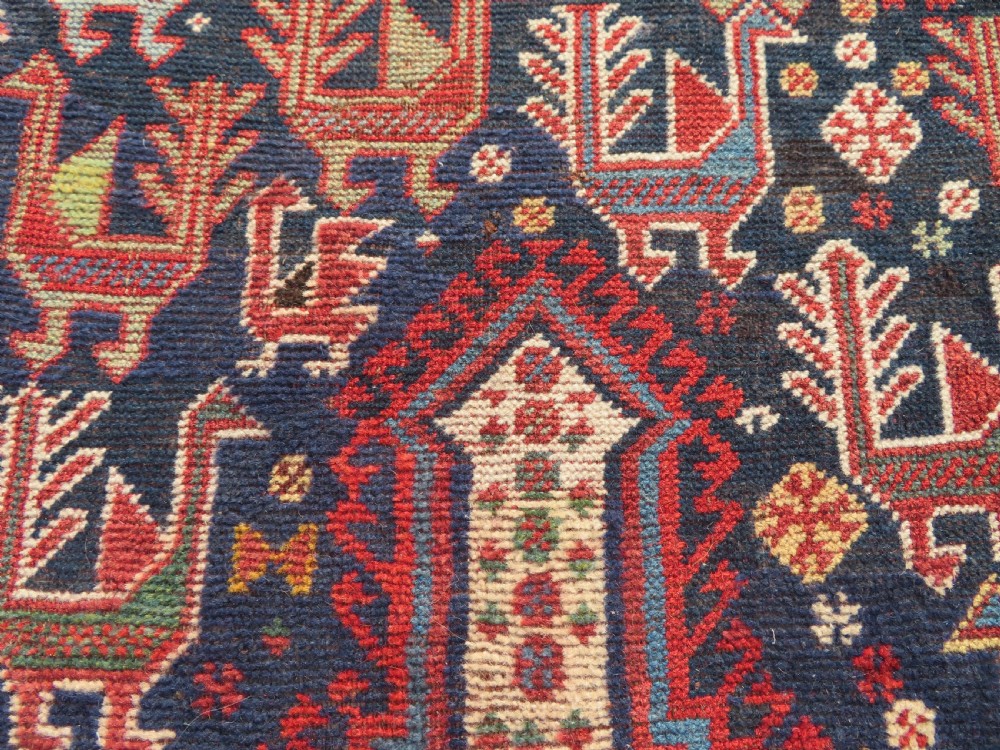 A late 19th-century Persian Qashqai hand-knotted wool rug featuring a navy blue field filled with stylized red peacock motifs, a central cream diamond medallion, and a wide red geometric border. View XXV