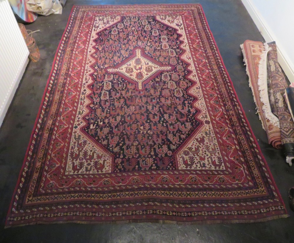 A late 19th-century Persian Qashqai hand-knotted wool rug featuring a navy blue field filled with stylized red peacock motifs, a central cream diamond medallion, and a wide red geometric border. View XXIX