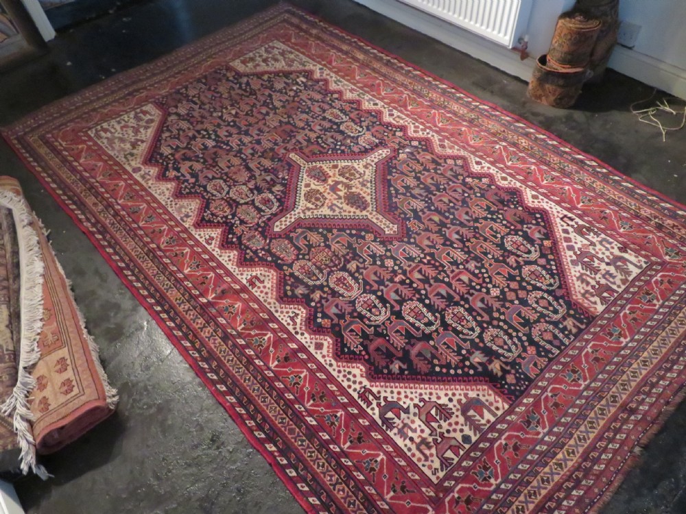 A late 19th-century Persian Qashqai hand-knotted wool rug featuring a navy blue field filled with stylized red peacock motifs, a central cream diamond medallion, and a wide red geometric border. View XXX