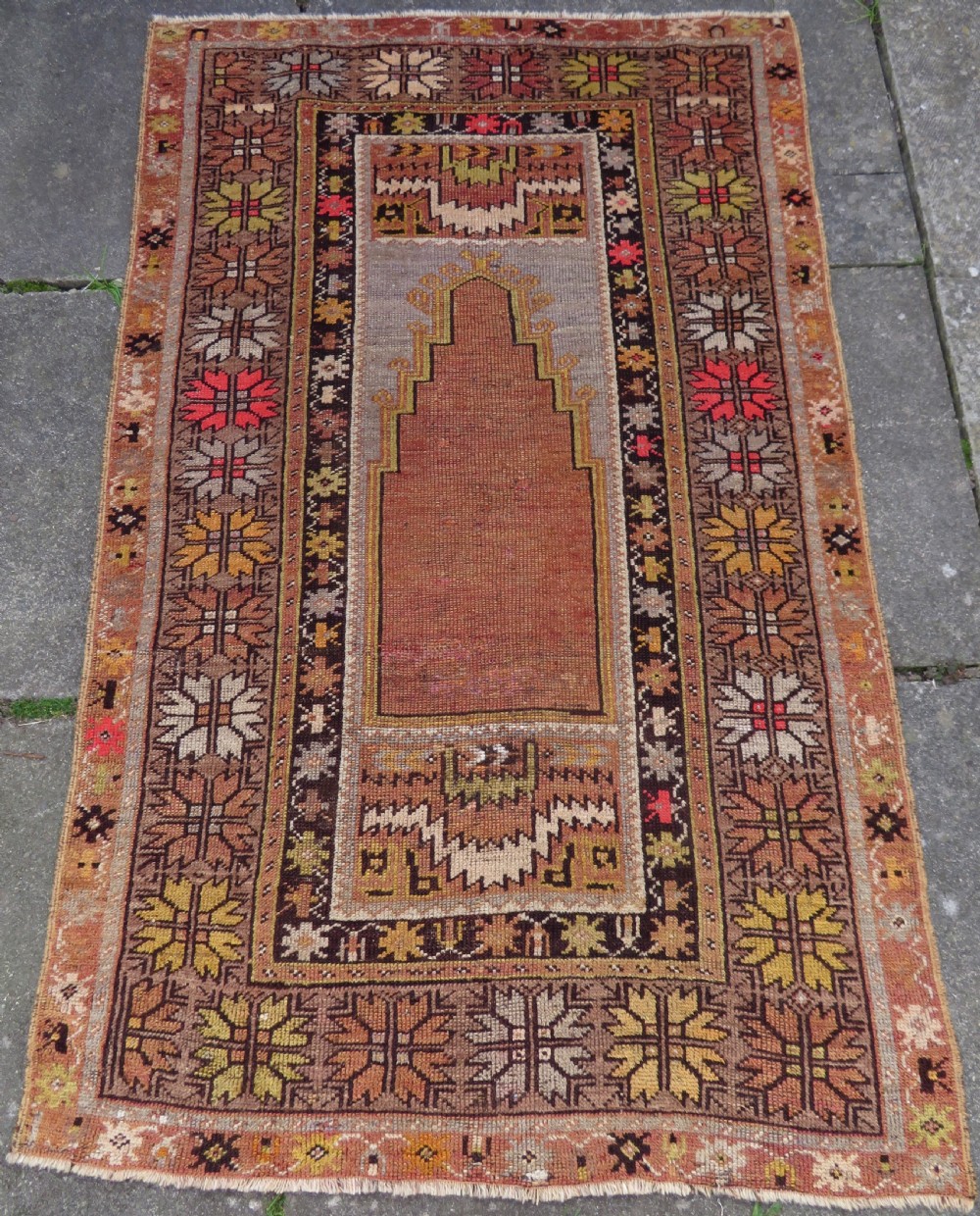 A late 19th-century hand-knotted Turkish Milas wool prayer rug featuring a central stepped mihrab niche surrounded by a wide geometric star pattern border in terracotta, gold, and earthy brown tones.