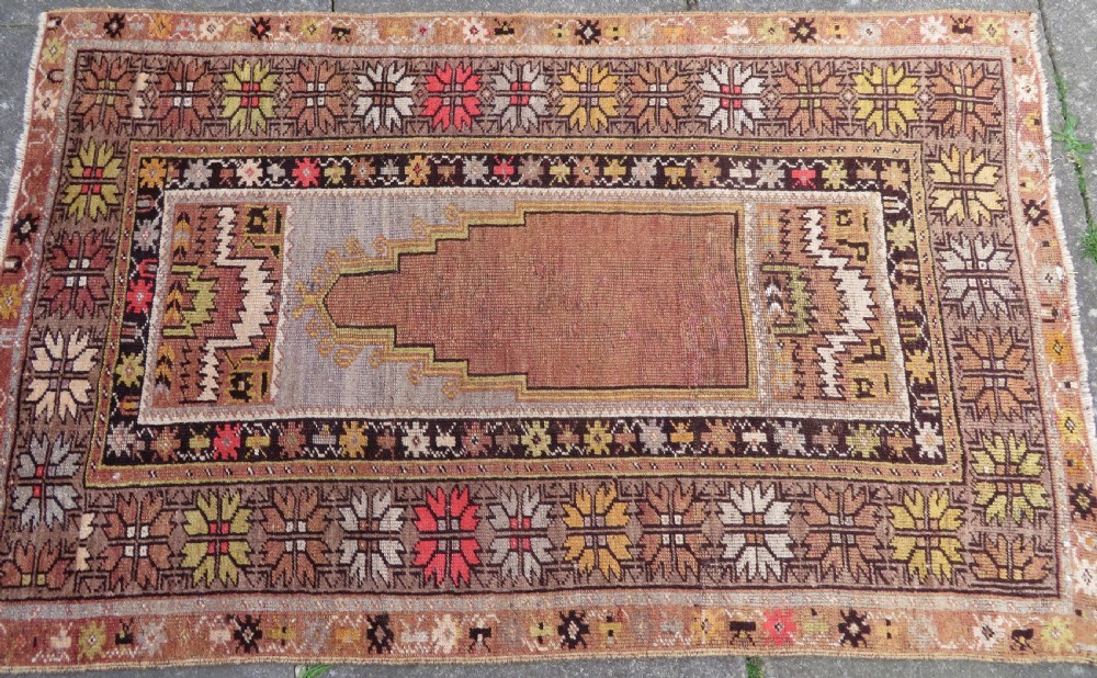 A late 19th-century hand-knotted Turkish Milas wool prayer rug featuring a central stepped mihrab niche surrounded by a wide geometric star pattern border in terracotta, gold, and earthy brown tones. View III