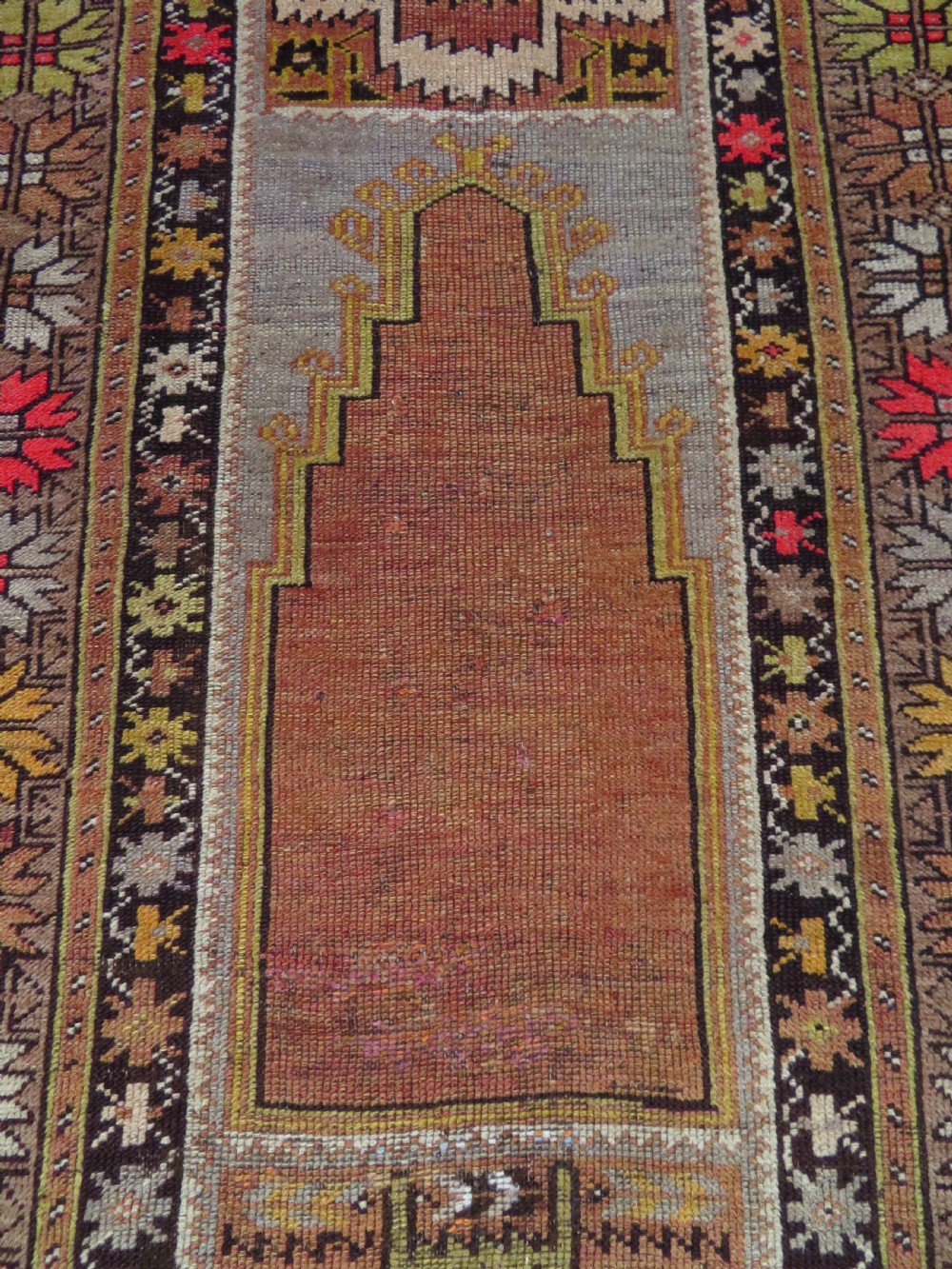 A late 19th-century hand-knotted Turkish Milas wool prayer rug featuring a central stepped mihrab niche surrounded by a wide geometric star pattern border in terracotta, gold, and earthy brown tones. View IV