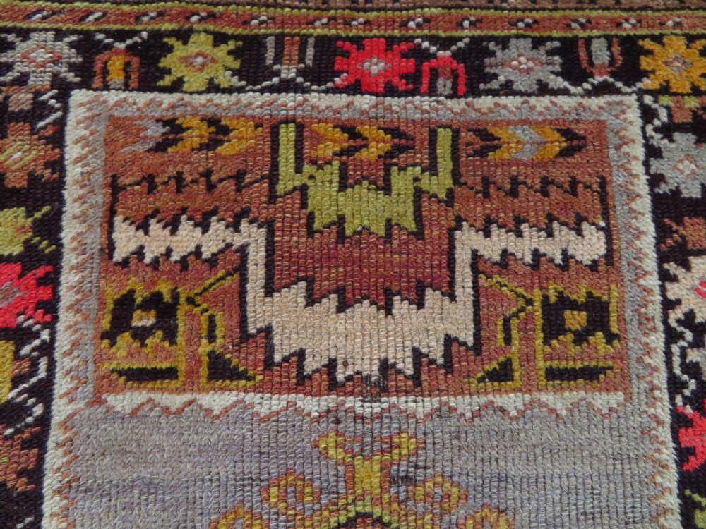 A late 19th-century hand-knotted Turkish Milas wool prayer rug featuring a central stepped mihrab niche surrounded by a wide geometric star pattern border in terracotta, gold, and earthy brown tones. View V
