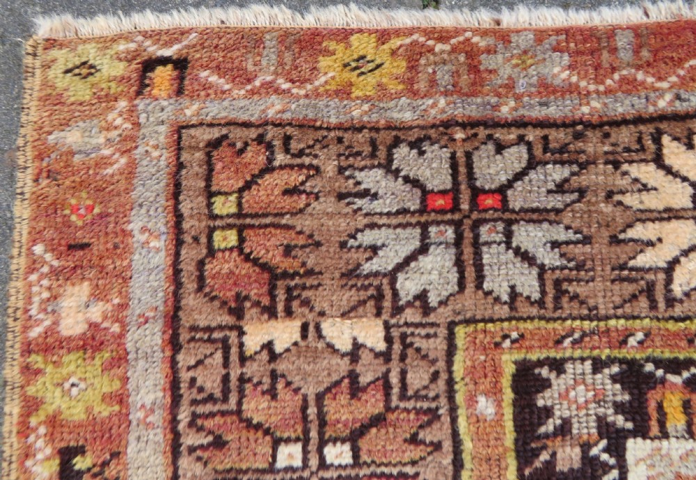 A late 19th-century hand-knotted Turkish Milas wool prayer rug featuring a central stepped mihrab niche surrounded by a wide geometric star pattern border in terracotta, gold, and earthy brown tones. View VI