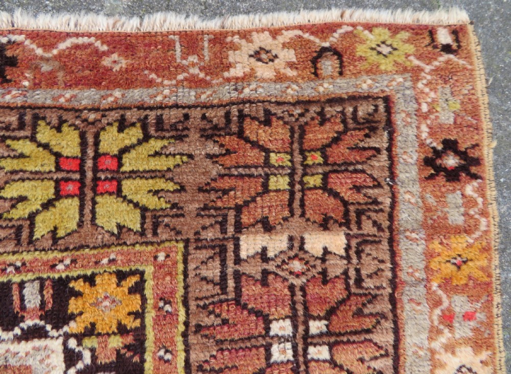 A late 19th-century hand-knotted Turkish Milas wool prayer rug featuring a central stepped mihrab niche surrounded by a wide geometric star pattern border in terracotta, gold, and earthy brown tones. View VII