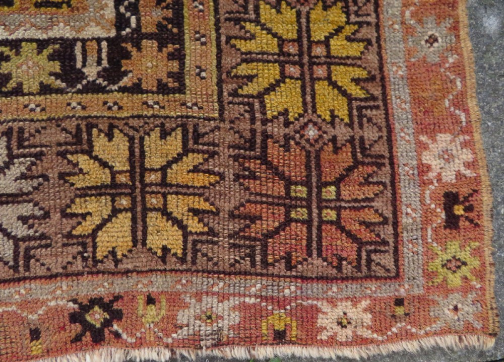 A late 19th-century hand-knotted Turkish Milas wool prayer rug featuring a central stepped mihrab niche surrounded by a wide geometric star pattern border in terracotta, gold, and earthy brown tones. View X