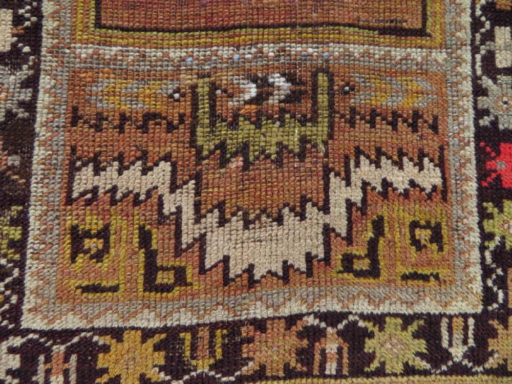A late 19th-century hand-knotted Turkish Milas wool prayer rug featuring a central stepped mihrab niche surrounded by a wide geometric star pattern border in terracotta, gold, and earthy brown tones. View XI