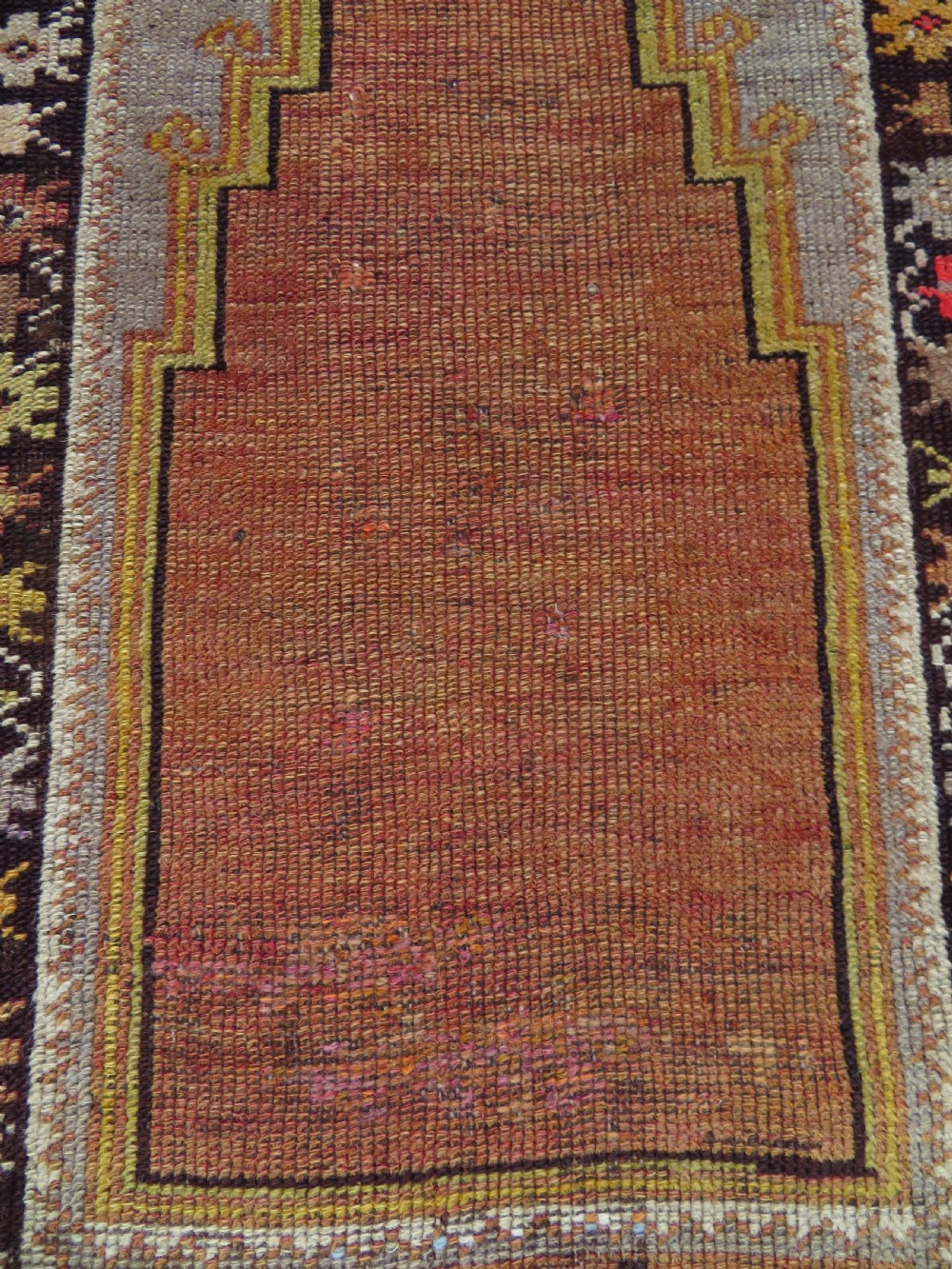 A late 19th-century hand-knotted Turkish Milas wool prayer rug featuring a central stepped mihrab niche surrounded by a wide geometric star pattern border in terracotta, gold, and earthy brown tones. View XII