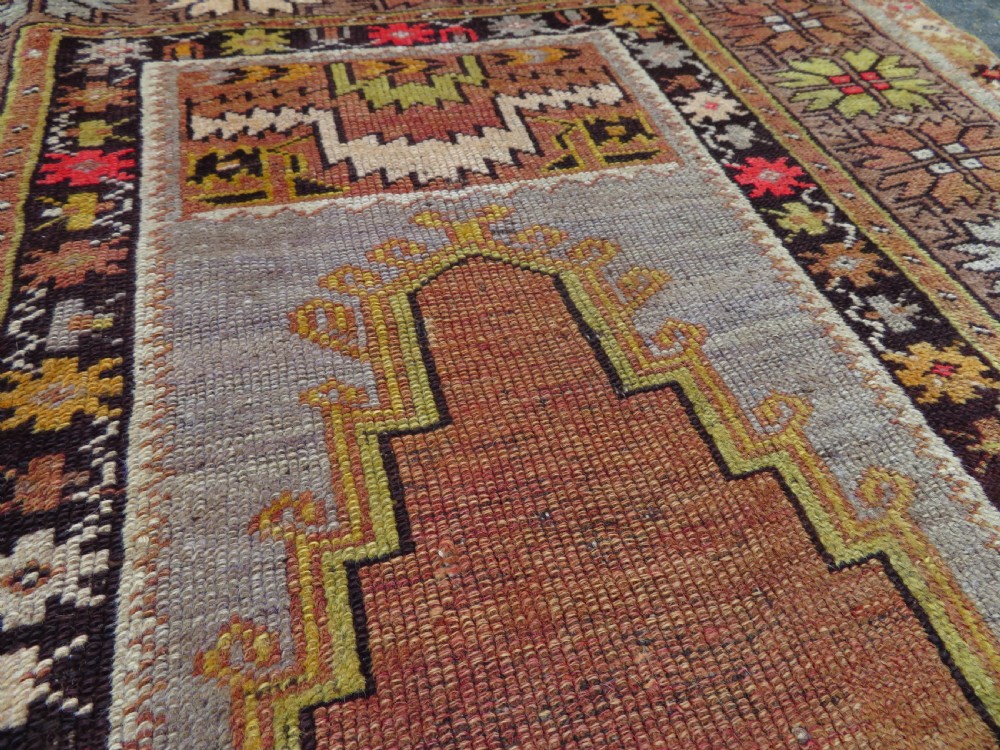 A late 19th-century hand-knotted Turkish Milas wool prayer rug featuring a central stepped mihrab niche surrounded by a wide geometric star pattern border in terracotta, gold, and earthy brown tones. View XIII