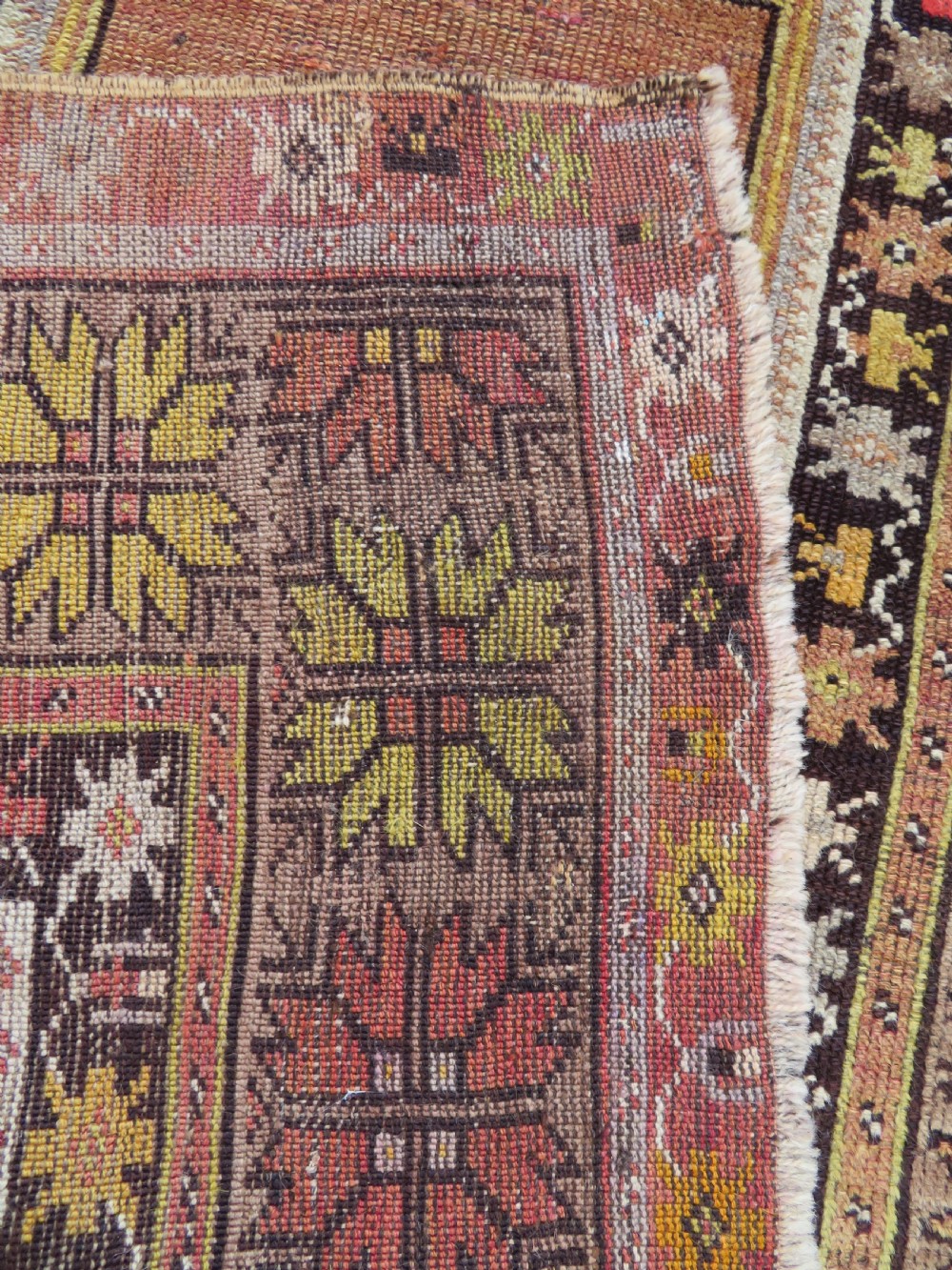 A late 19th-century hand-knotted Turkish Milas wool prayer rug featuring a central stepped mihrab niche surrounded by a wide geometric star pattern border in terracotta, gold, and earthy brown tones. View XIV