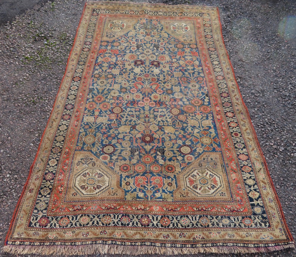 An antique Persian Qashqai Millefleurs wool rug featuring a central arch field filled with dense floral motifs in navy blue, terracotta, and ochre tones.