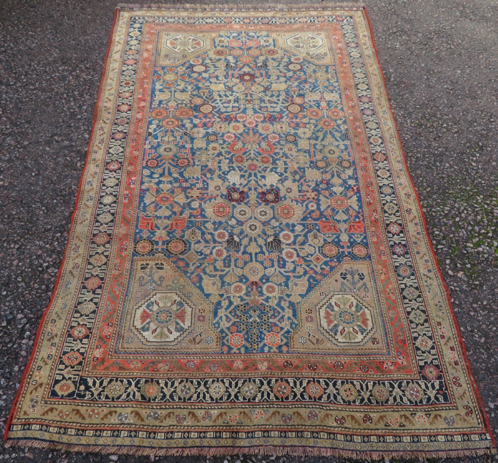 An antique Persian Qashqai Millefleurs wool rug featuring a central arch field filled with dense floral motifs in navy blue, terracotta, and ochre tones. View II