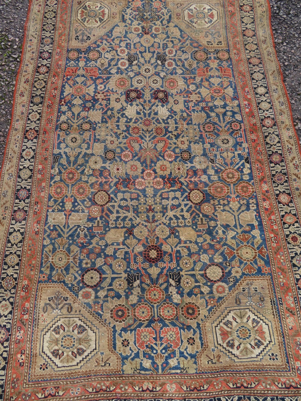 An antique Persian Qashqai Millefleurs wool rug featuring a central arch field filled with dense floral motifs in navy blue, terracotta, and ochre tones. View III
