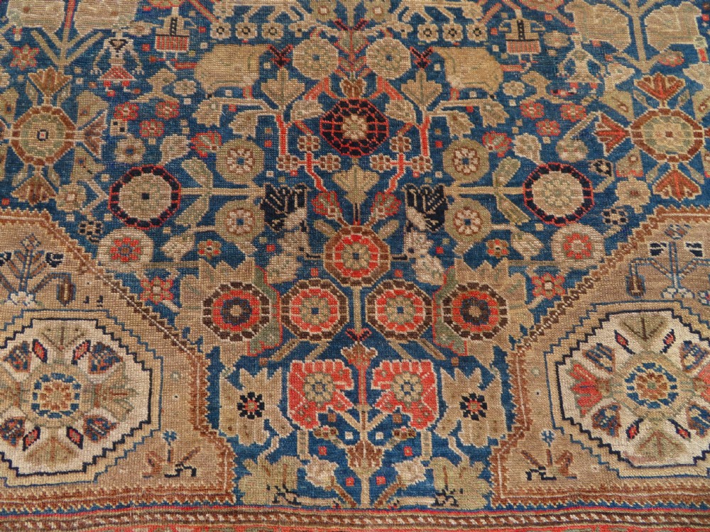 An antique Persian Qashqai Millefleurs wool rug featuring a central arch field filled with dense floral motifs in navy blue, terracotta, and ochre tones. View IV
