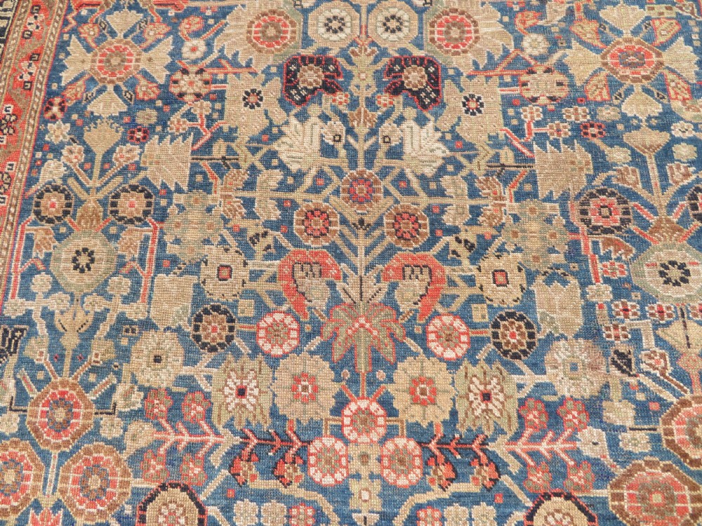 An antique Persian Qashqai Millefleurs wool rug featuring a central arch field filled with dense floral motifs in navy blue, terracotta, and ochre tones. View V