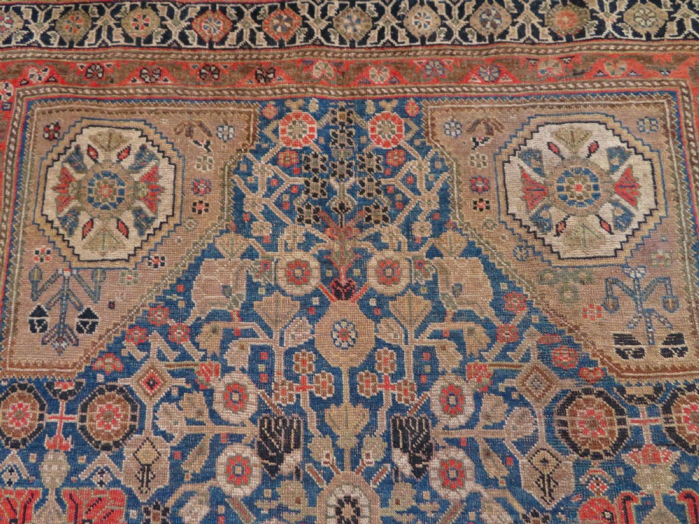 An antique Persian Qashqai Millefleurs wool rug featuring a central arch field filled with dense floral motifs in navy blue, terracotta, and ochre tones. View VI