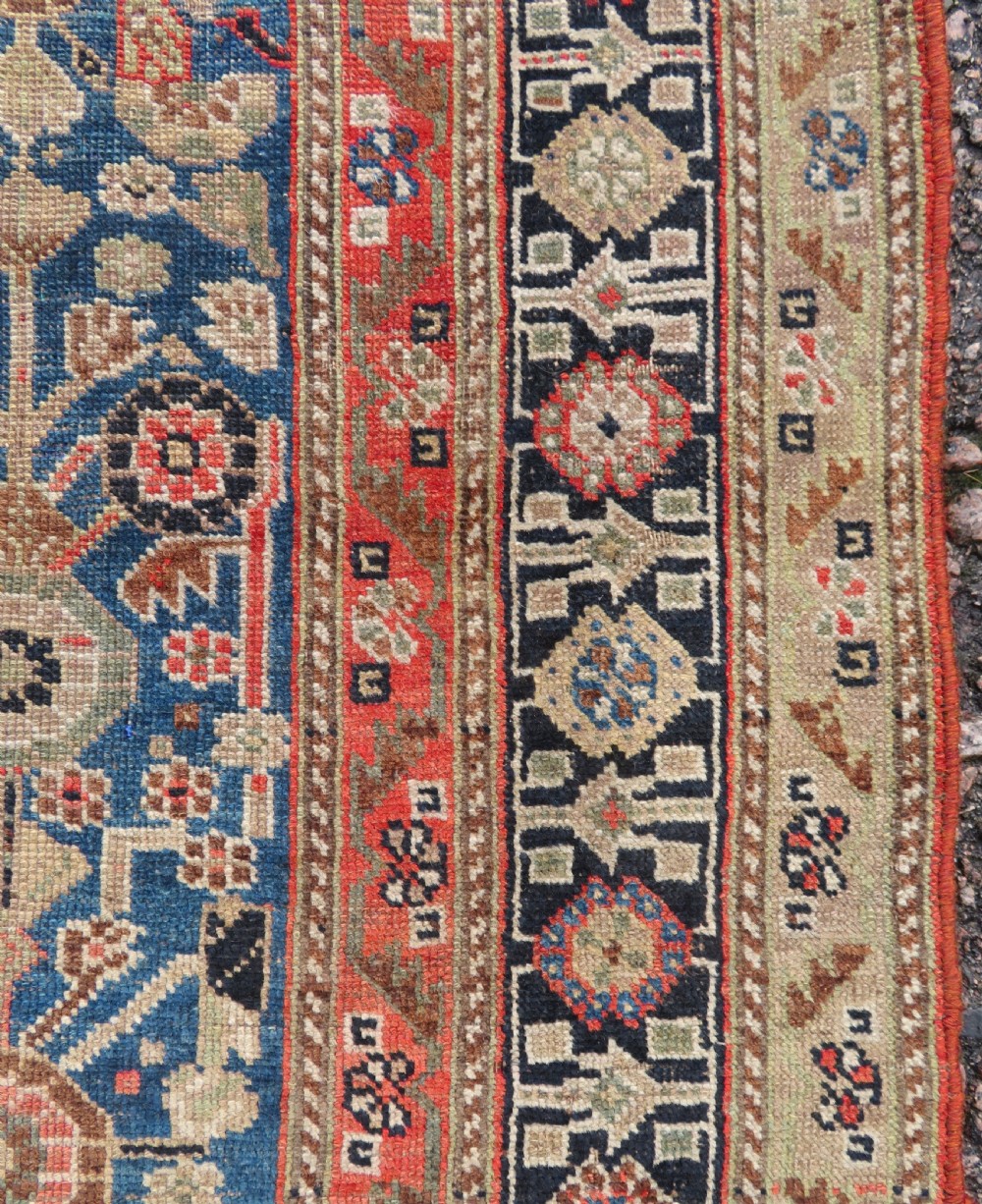 An antique Persian Qashqai Millefleurs wool rug featuring a central arch field filled with dense floral motifs in navy blue, terracotta, and ochre tones. View VIII