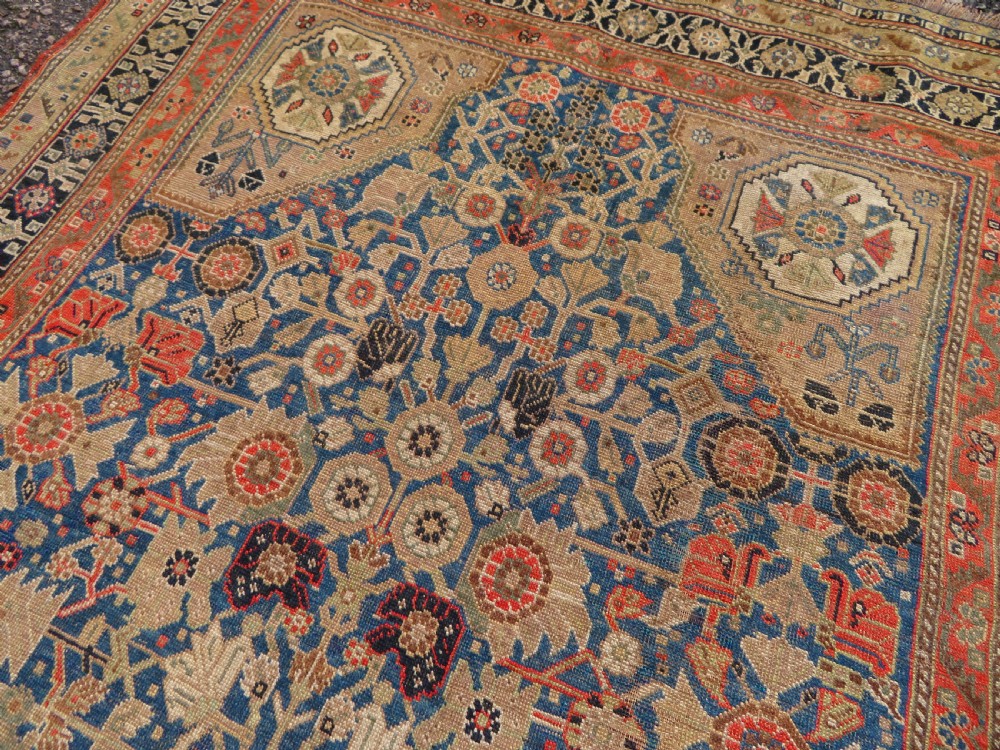 An antique Persian Qashqai Millefleurs wool rug featuring a central arch field filled with dense floral motifs in navy blue, terracotta, and ochre tones. View XV