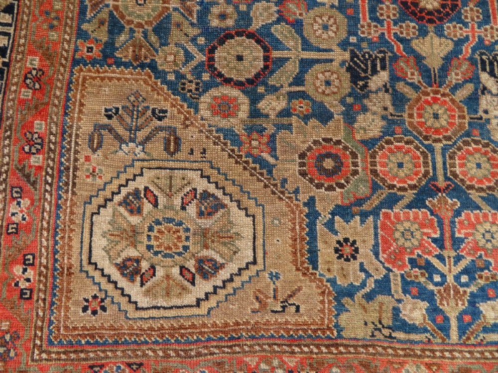 An antique Persian Qashqai Millefleurs wool rug featuring a central arch field filled with dense floral motifs in navy blue, terracotta, and ochre tones. View XVII