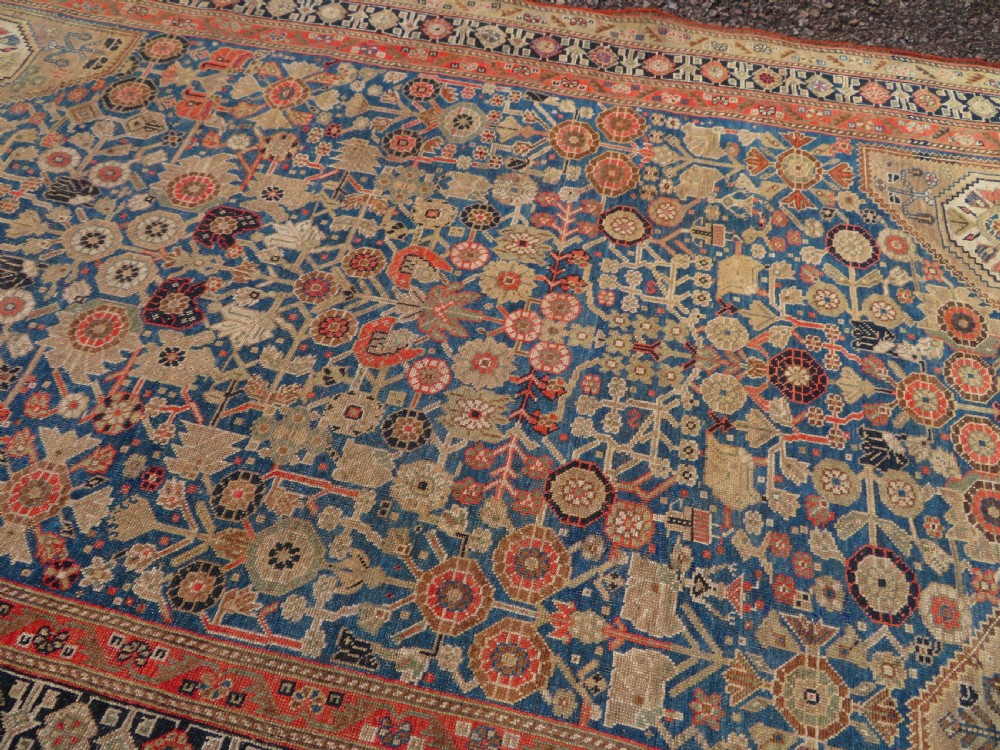An antique Persian Qashqai Millefleurs wool rug featuring a central arch field filled with dense floral motifs in navy blue, terracotta, and ochre tones. View XIX