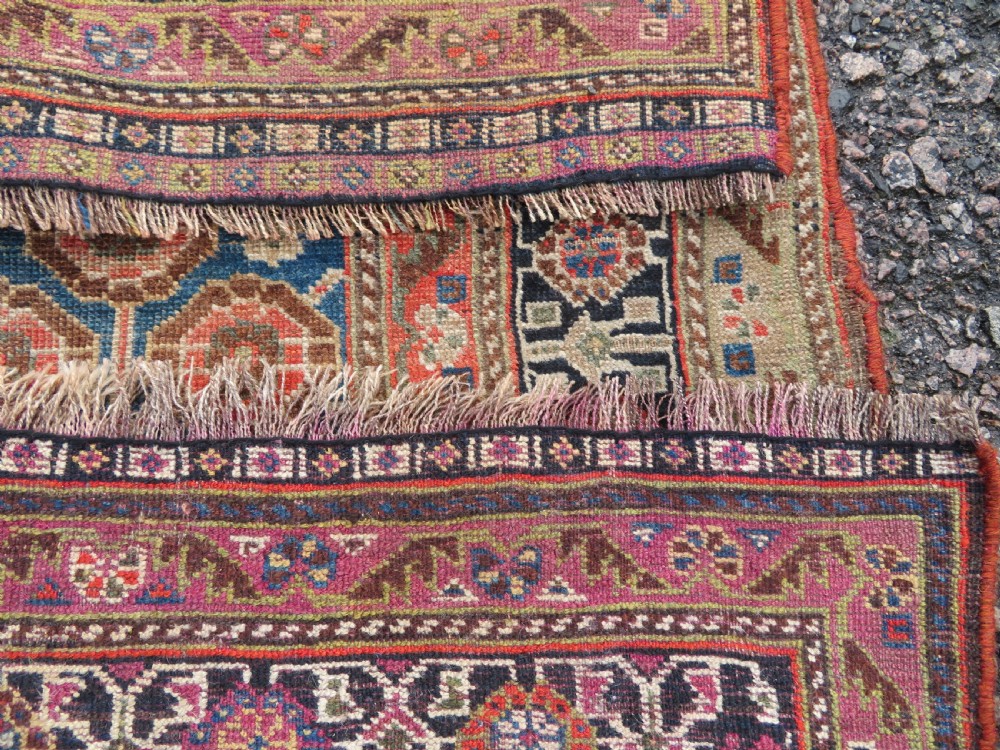 An antique Persian Qashqai Millefleurs wool rug featuring a central arch field filled with dense floral motifs in navy blue, terracotta, and ochre tones. View XXI