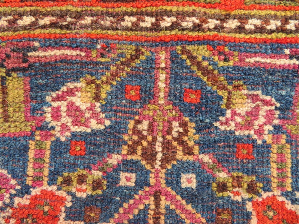 An antique Persian Qashqai Millefleurs wool rug featuring a central arch field filled with dense floral motifs in navy blue, terracotta, and ochre tones. View XXII