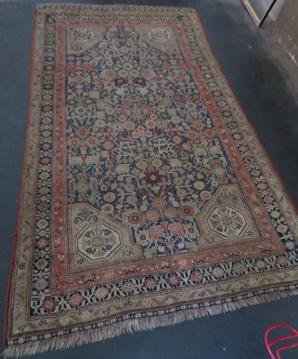 An antique Persian Qashqai Millefleurs wool rug featuring a central arch field filled with dense floral motifs in navy blue, terracotta, and ochre tones. View XXIV