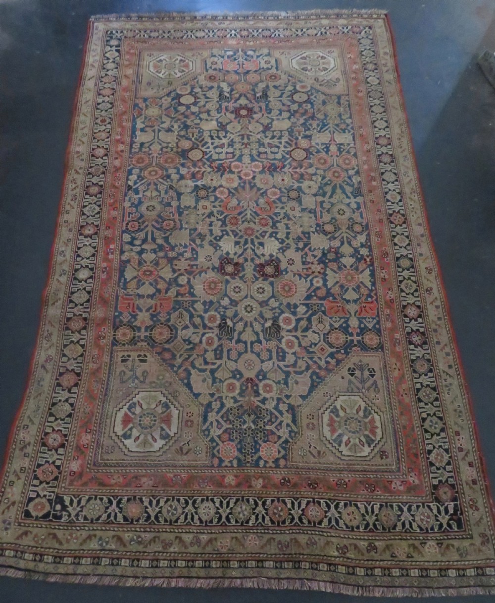 An antique Persian Qashqai Millefleurs wool rug featuring a central arch field filled with dense floral motifs in navy blue, terracotta, and ochre tones. View XXV