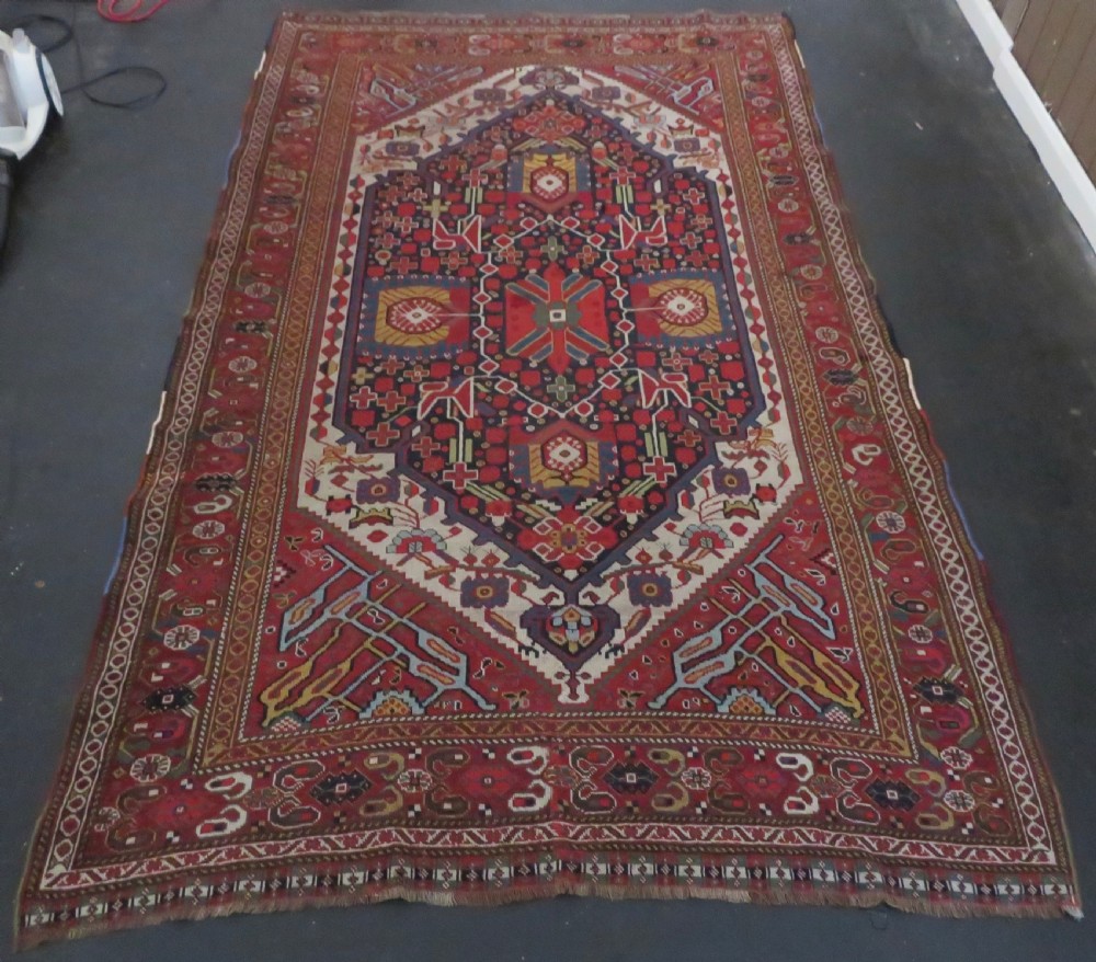 An antique hand-woven Persian Khamseh wool rug featuring a central geometric medallion with tribal bird motifs in red, navy blue, and ivory tones.