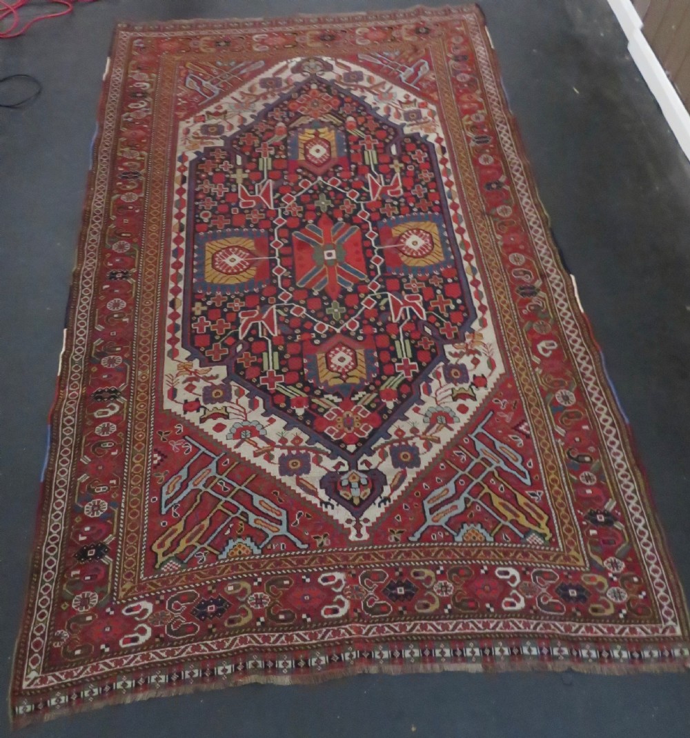 An antique hand-woven Persian Khamseh wool rug featuring a central geometric medallion with tribal bird motifs in red, navy blue, and ivory tones. View II