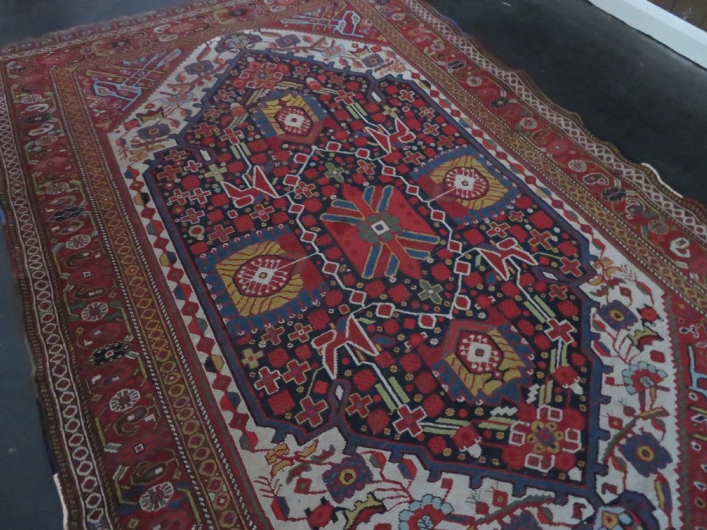 An antique hand-woven Persian Khamseh wool rug featuring a central geometric medallion with tribal bird motifs in red, navy blue, and ivory tones. View III