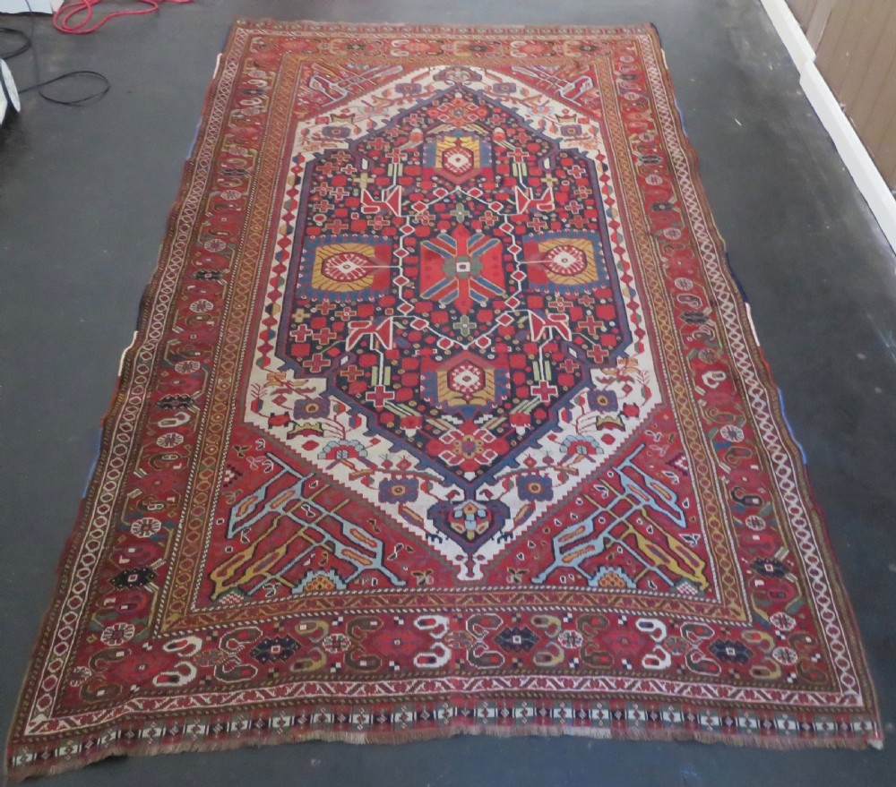 An antique hand-woven Persian Khamseh wool rug featuring a central geometric medallion with tribal bird motifs in red, navy blue, and ivory tones. View V