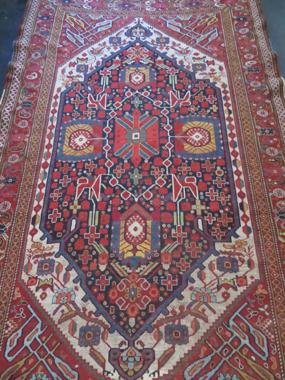 An antique hand-woven Persian Khamseh wool rug featuring a central geometric medallion with tribal bird motifs in red, navy blue, and ivory tones. View VI