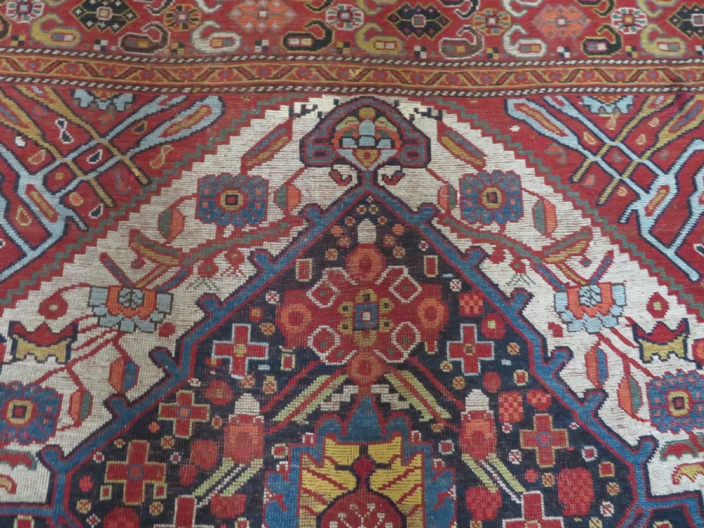 An antique hand-woven Persian Khamseh wool rug featuring a central geometric medallion with tribal bird motifs in red, navy blue, and ivory tones. View X