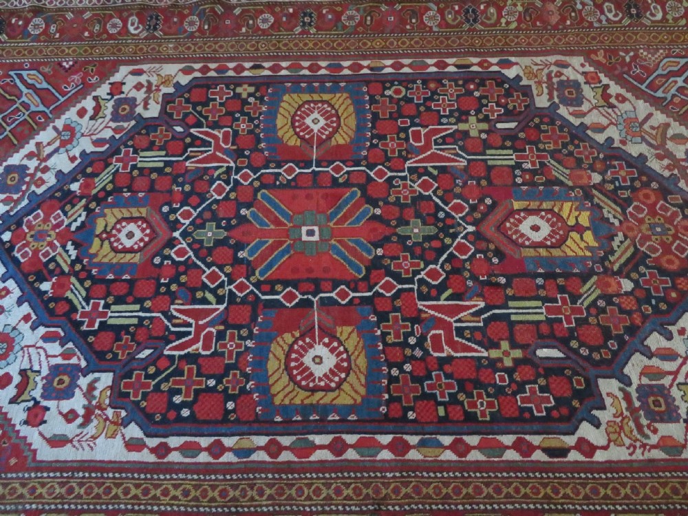 An antique hand-woven Persian Khamseh wool rug featuring a central geometric medallion with tribal bird motifs in red, navy blue, and ivory tones. View XIV