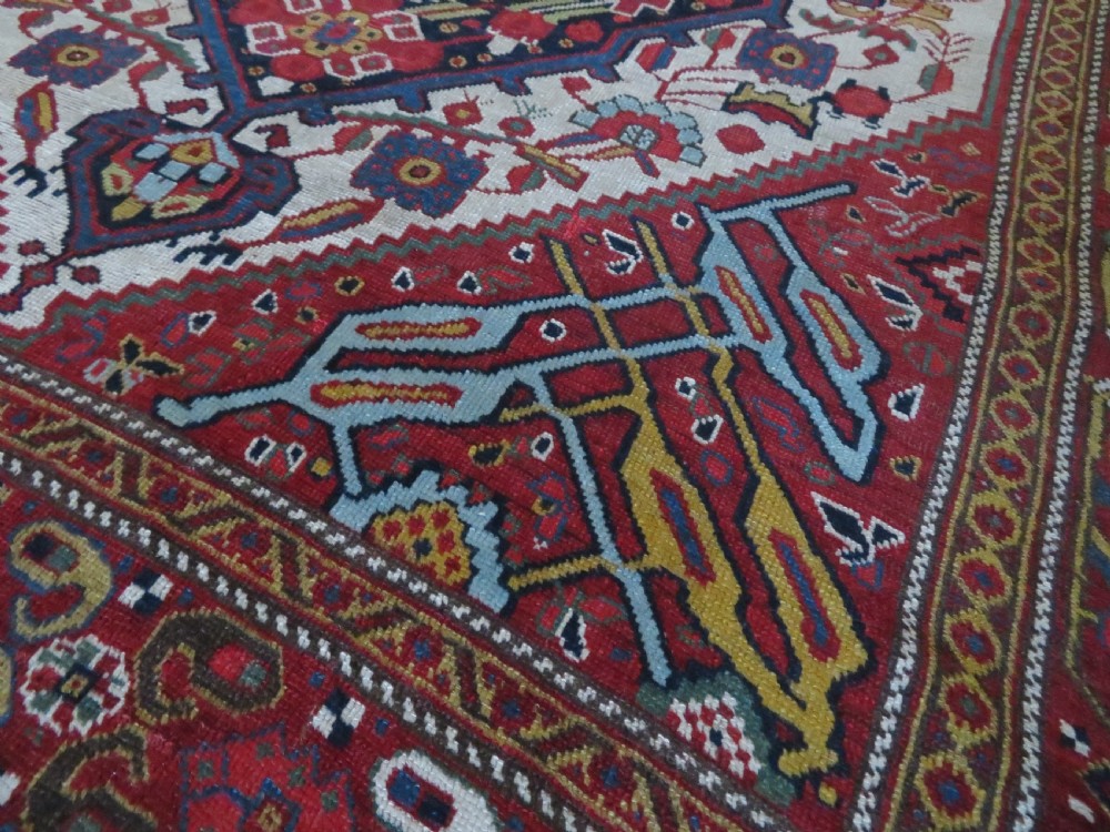 An antique hand-woven Persian Khamseh wool rug featuring a central geometric medallion with tribal bird motifs in red, navy blue, and ivory tones. View XV
