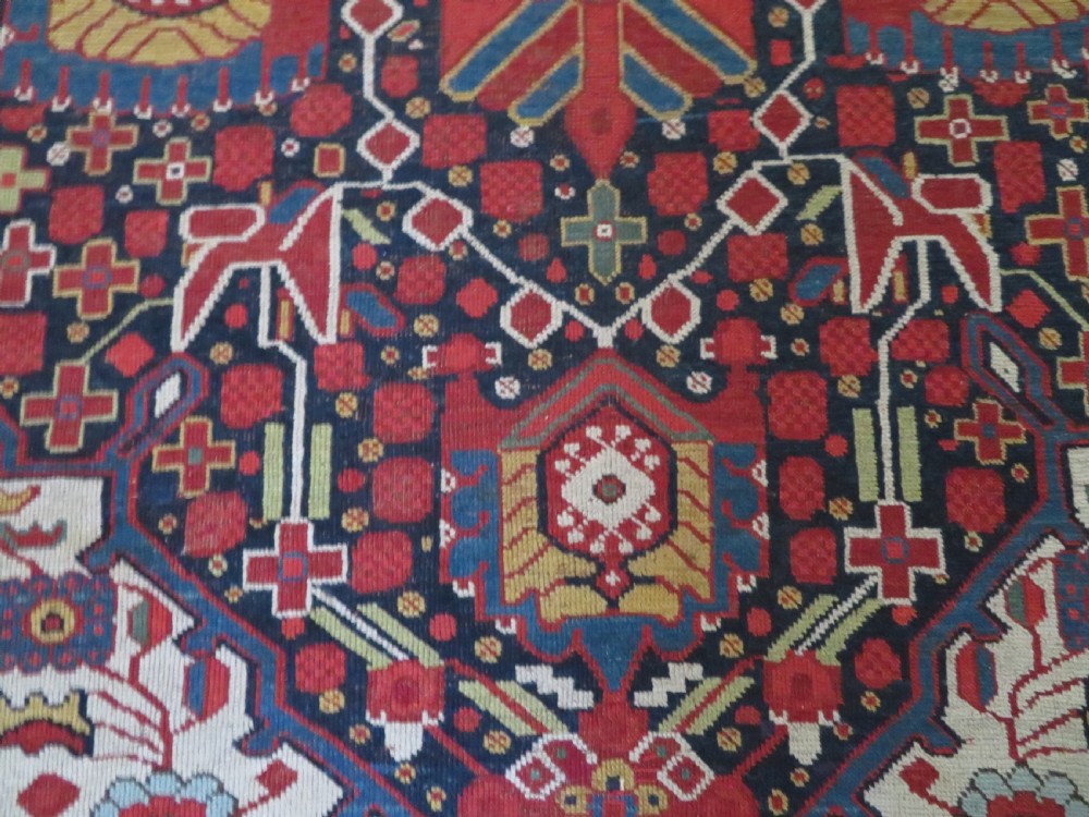 An antique hand-woven Persian Khamseh wool rug featuring a central geometric medallion with tribal bird motifs in red, navy blue, and ivory tones. View XVII