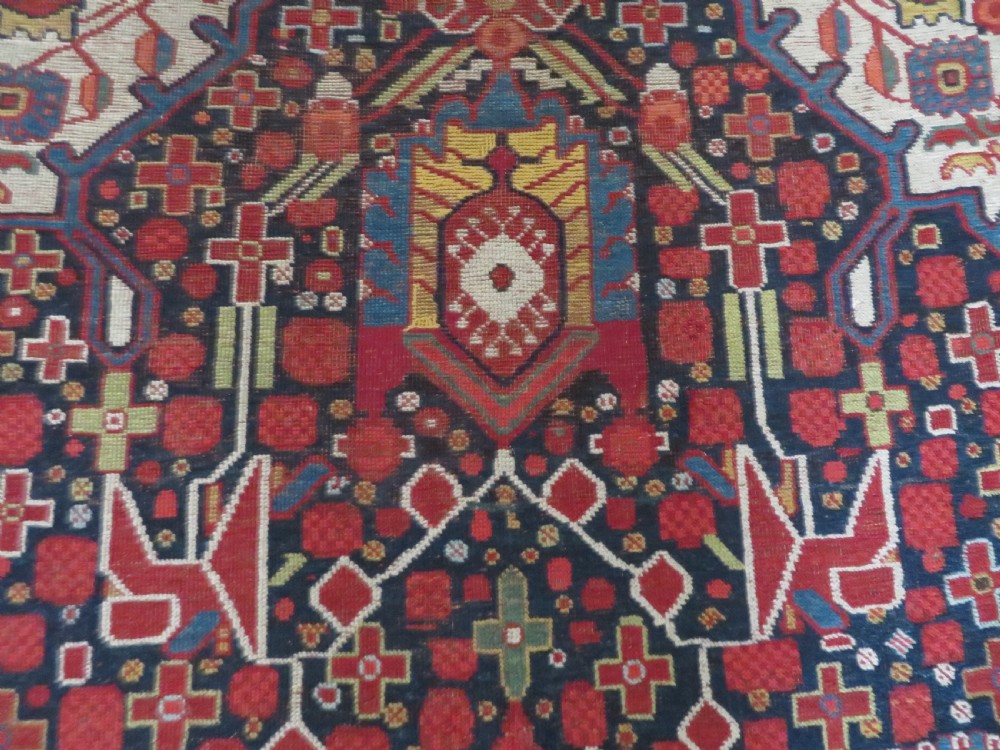 An antique hand-woven Persian Khamseh wool rug featuring a central geometric medallion with tribal bird motifs in red, navy blue, and ivory tones. View XVIII